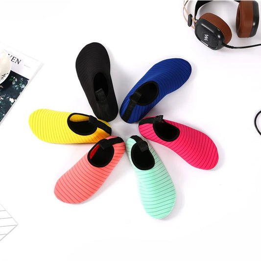 A collection of Drift Sock Shoes in various colors displayed in a circle on a white surface, with headphones and a book in the background.